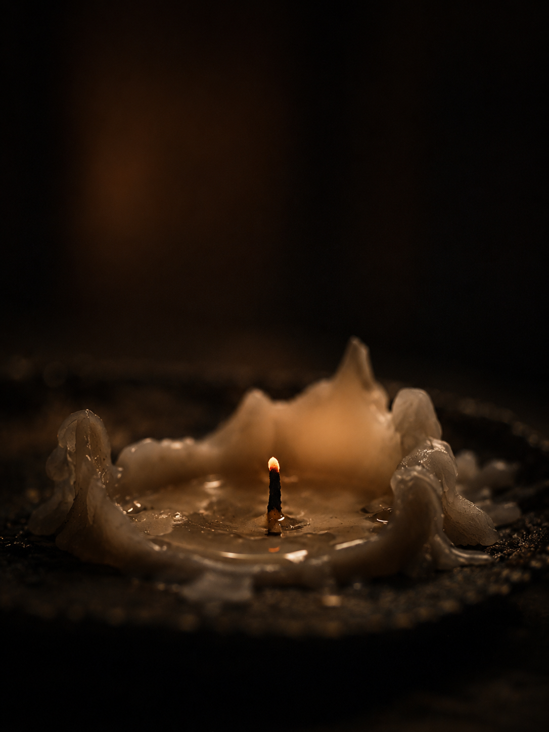 A candle burned down to a small pool of wax, the wick barely glowing